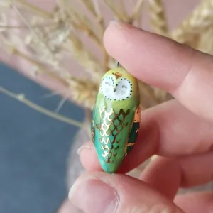 Macro shot of a tiny hand-painted green owl pendant with golden 14K scales and glaze