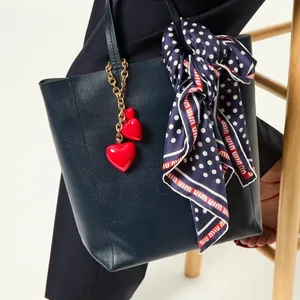 Dark blue leather tote bag featuring a red heart pendant and a polka dot silk scarf