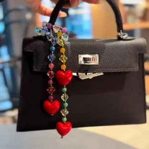 Detail of red heart charms and colorful beads on a black lychee texture handbag