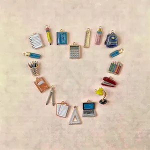 Enamel stationery charm set with laptop and backpack arranged in heart shape