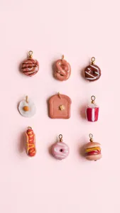 Flat lay of nine realistic food-shaped pendants with gold metal rings on pink background