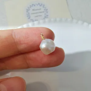 Close-up of handmade baroque pearl pendant with gold wire wrapping held by hand