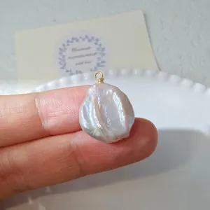 Macro detail of a baroque pearl pendant with gold wire wrap held on a fingertip