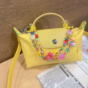 Detail of yellow mini nylon bag featuring colorful smiley face and heart bead charms