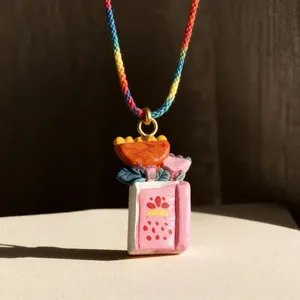 Collar con colgante de libro rosa con flores de colores y cordón tejido arcoíris