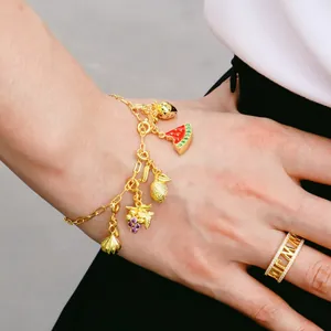 Détail d'un bracelet doré aux breloques de fruits en émail et bague sertie de zircons