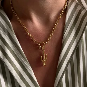 Close-up of golden cactus pendant on rolo chain worn over a striped shirt