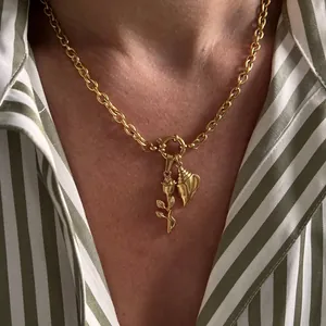 Detail of gold necklace featuring rose and seashell charms on a striped shirt background