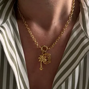 Detail of gold palm tree pendant and textured charm on chunky link chain necklace