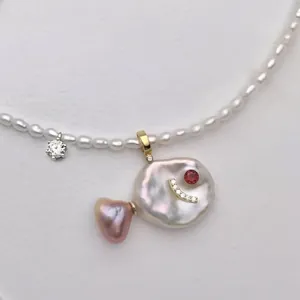 Detailed shot of fish-shaped pearl pendant necklace with red gemstone and gold accents