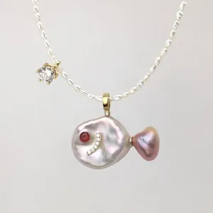 Macro shot of fish-shaped gold pendant with baroque pearl, ruby eye and diamond accents
