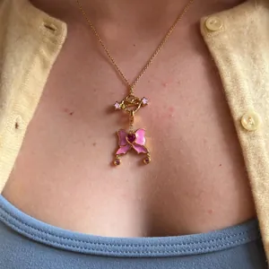 Detailaufnahme einer goldenen Herzenskette mit rosa Glitzerschleife an einem Model