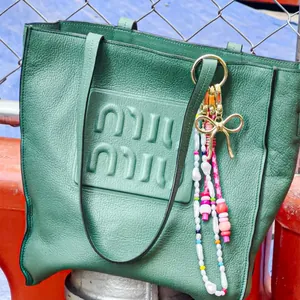 Detail of green pebble leather tote bag featuring colorful bead charms and bow ornament
