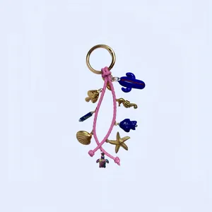 Détail d'un cordon tressé rose avec breloques marines dorées comme hippocampe et coquillage