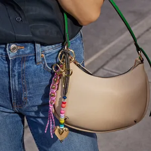 Detailed view of colorful beaded charms with gold heart and pink woven knot on beige bag