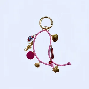 Détail d'un pendentif en cuir tressé rose avec coquillages dorés et perles en céramique