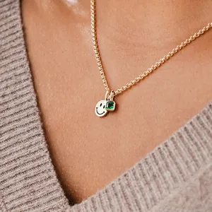 Detail einer Goldkette mit Smiley-Plakette und einem grünen Smaragd-Anhänger am Modell