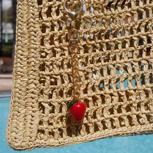 Detail van een vintage aardbeien tassenhanger met gouden ketting aan een rieten tas