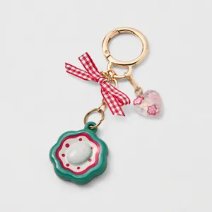 Détail du porte-clés avec fleur verte, nœud en tissu et pendentif en forme de cœur rose