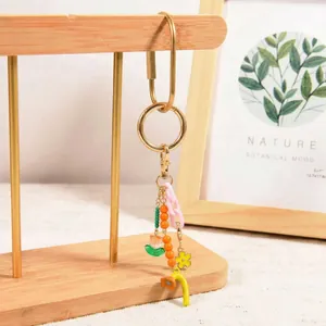 Close-up of golden tulip keychain with orange beads and pink chain on wood stand