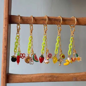 Details von fünf Taschenanhängern mit Obstmotiven, neon-grünen Ketten und goldenen Ringen