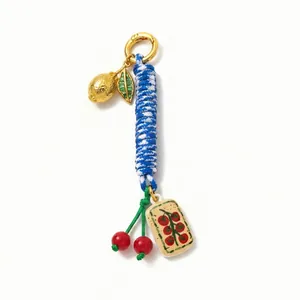Close-up of woven blue rope keychain with golden lemon and red cherry charms
