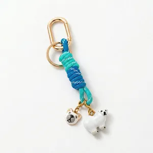Detalle del llavero dorado con colgantes de oso polar y cordón trenzado azul y verde