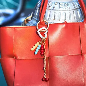DIY charm keychain with colorful beads and cherry pendants on a red woven bag