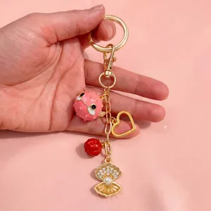 Vue détaillée d'un porte-clés doré avec pendentif poisson-globe rose et coquillage perlé