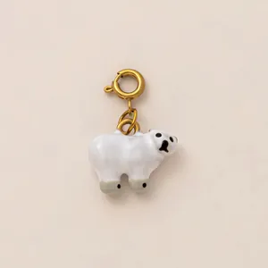 Detalle de un dije de oso polar blanco con cierre de resorte dorado y detalles de esmalte negro