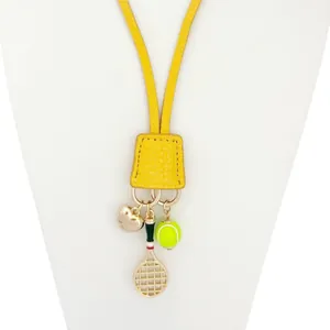 Détail d'un bijou de sac en cuir jaune avec cœur doré et raquette de tennis