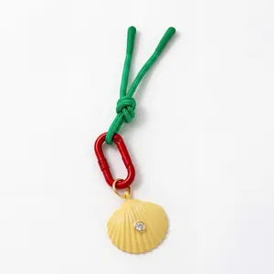 Detail of colorful charm featuring a green woven cord, red ring, and yellow shell pendant