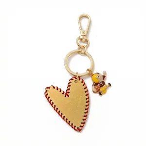 Detail of heart pendant with red stitching, gold lobster clasp and sports mascot charm