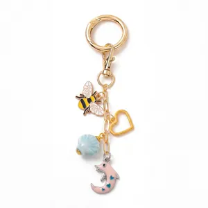 Détail de porte-clés doré DIY avec breloque abeille, perle bleue et pendentif dauphin lune
