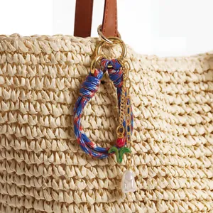Detail of red tulip pendant and pearl charm on a woven tricolor cord bag accessory