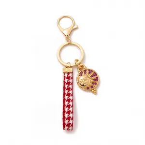 Detail of golden keychain with purple gemstones and red houndstooth ribbon charm