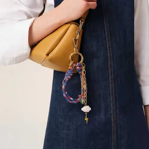 Colorful woven rope keychain with enamel flower and gold lightning charm on yellow bag