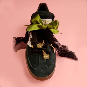Detail of black suede sneaker with green ribbon bow, lace trim and golden charms