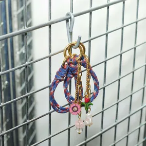 Detail of woven rope keychain with enamel flower, baroque pearl and gold accents