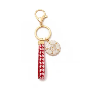 Close-up of golden keychain with red houndstooth ribbon and white flower charm pendant