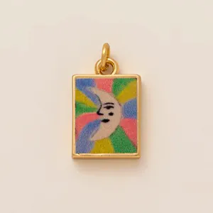 Detail of a rectangular golden charm with a rainbow moon face design and hanging ring