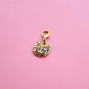 Detail of golden cat pendant with white enamel inlay and lobster clasp on pink background