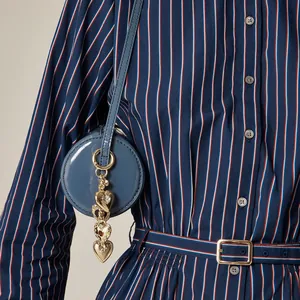 Marineblaue runde Lackledertasche mit goldenem Herzanhänger am gestreiften Kleid