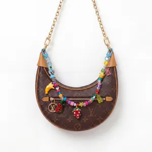 Detail van monogram handtas met kleurrijke fruitbedels en een gouden schouderketting