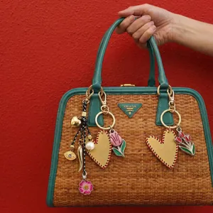 Close-up of heart charms and floral accessories on a woven bag with green leather trim
