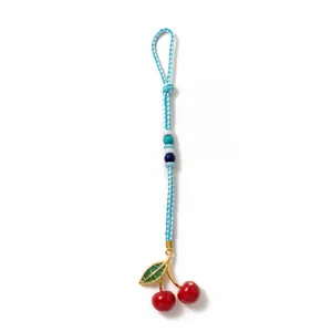 Detail of handmade woven cherry bag charm with red fruit and blue beaded braided rope
