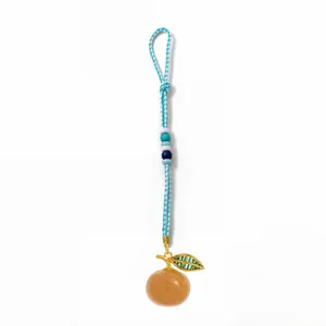 Detailed close-up of handmade woven keychain with blue cord and orange fruit resin pendant