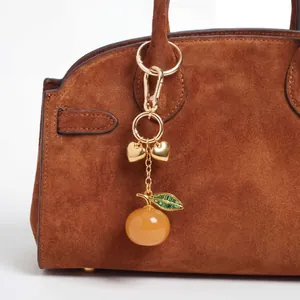 Close-up of luxury gold heart and amber peach charm on a brown suede handbag