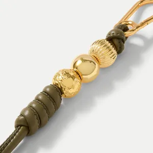 Makro-Detail des olivgrünen Lederbandes mit goldenen Perlen und einem Metallhaken