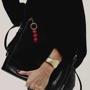 Close-up of three red resin hearts bag charm and elegant matte gold wide cuff bracelet